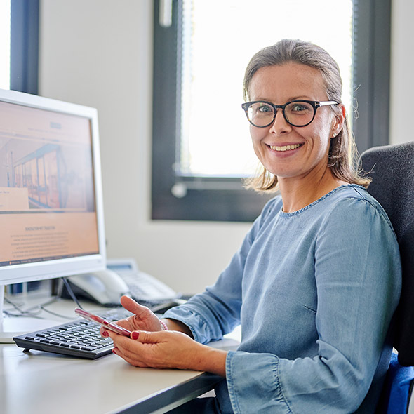 Eine Frau mit Brille sitzt am Schreibtisch vor einem Computer